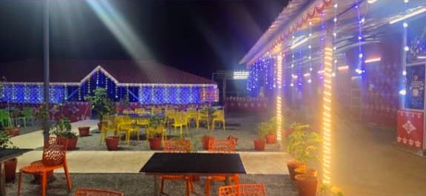 The courtyard of Brindavanam after dark, lit by strings of blue and warm white bulbs hung under the veranda, with chairs set out on the terrace.